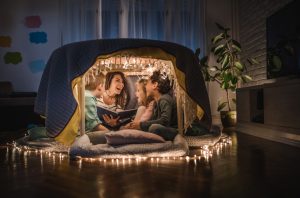 Happy mother sitting with her children and adopted children in a tent at home and having fun while reading them a book.