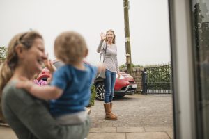 A women waves goodbye to her mother and son from across the street as she leaves the house.
