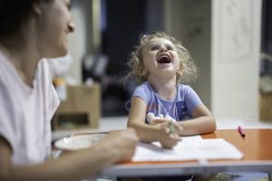Mother spending evening together with her little girl, drawing and laughing.