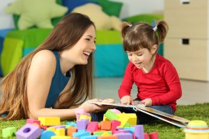 Mother and toddler playing together with a book lying on the floor in the bedroom at home with a colorful background